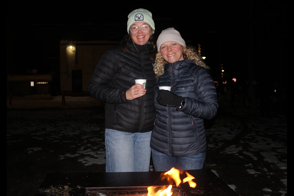 From left, friends Camille and Roxy warm up by the fire while they wait for fireworks to start (Gillian Francis/The Free Press)