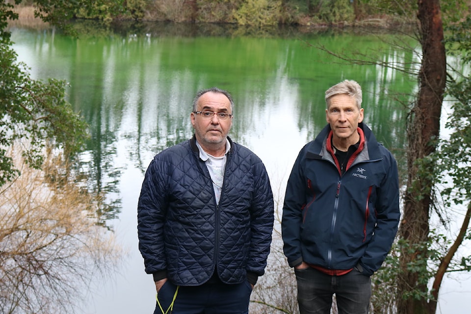 Clayton Leachman and Brian Belcher stand in front of Langford Lake – the polluting sediment resting on the bottom of the lake giving it a bright green appearance.