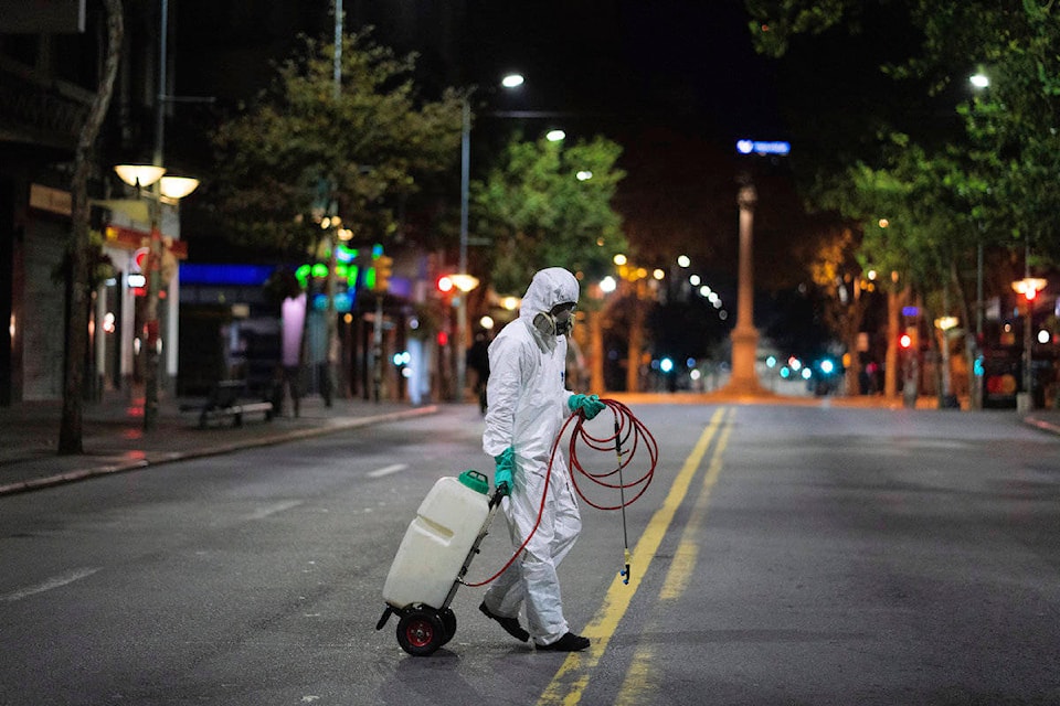 A city worker crosses a main avenue to disinfect a bus stop amid the spread of new coronavirus in Montevideo, Uruguay, early Monday, April 20, 2020. (AP Photo/Matilde Campodonico)