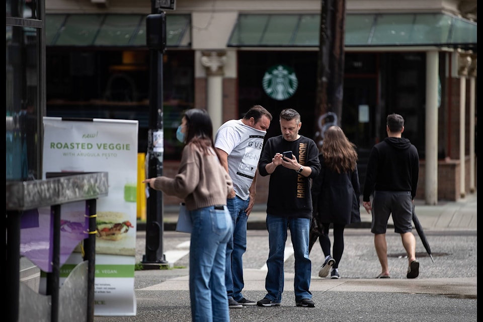 A man covers his mouth and nose with his T-shirt as he leans in closely to another man speaking and showing something on his phone, in Vancouver, on Sunday, May 17, 2020. THE CANADIAN PRESS/Darryl Dyck