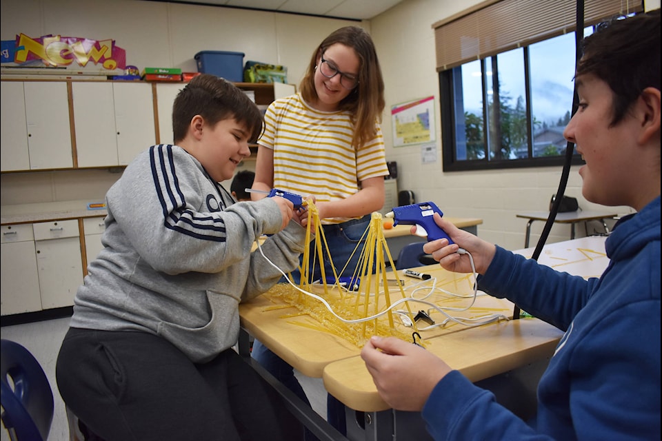 Nyah Tiessen, left, Jaxson Hartmann and Connor Hidalgo had spent about an hour and a half on their bridge design and were busy adding spaghetti sticks to connect the beams of their bridge. (Emelie Peacock/Hope Standard)