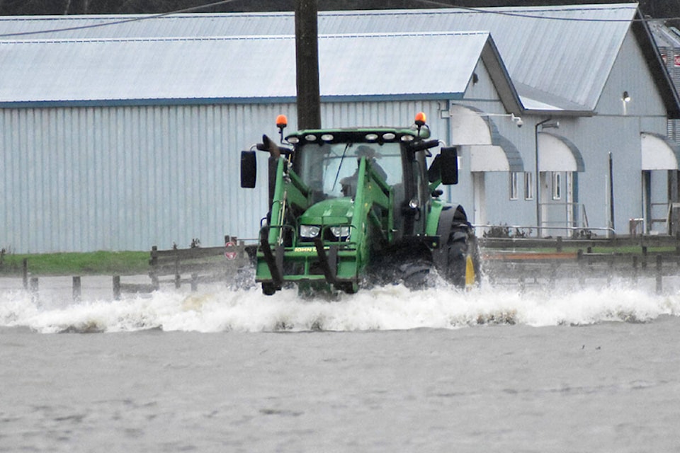 A farmer off of North Parallel Road drives his tractor through water. (Ben Lypka/Abbotsford News)