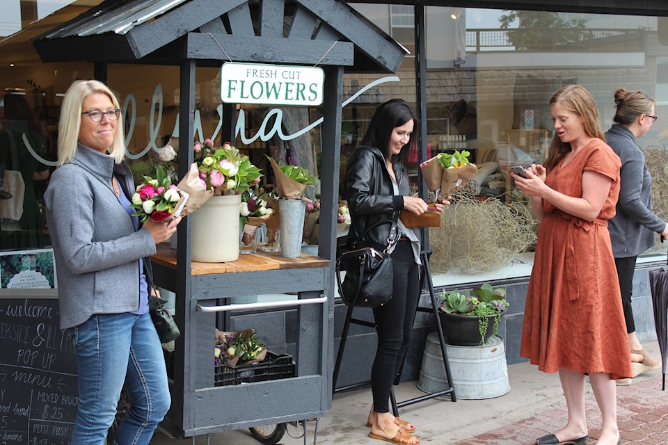 Anna Gauthier, right, sells fresh cut flowers to customers outside Illyria on Main Street July 10. (Thom Barker photo)