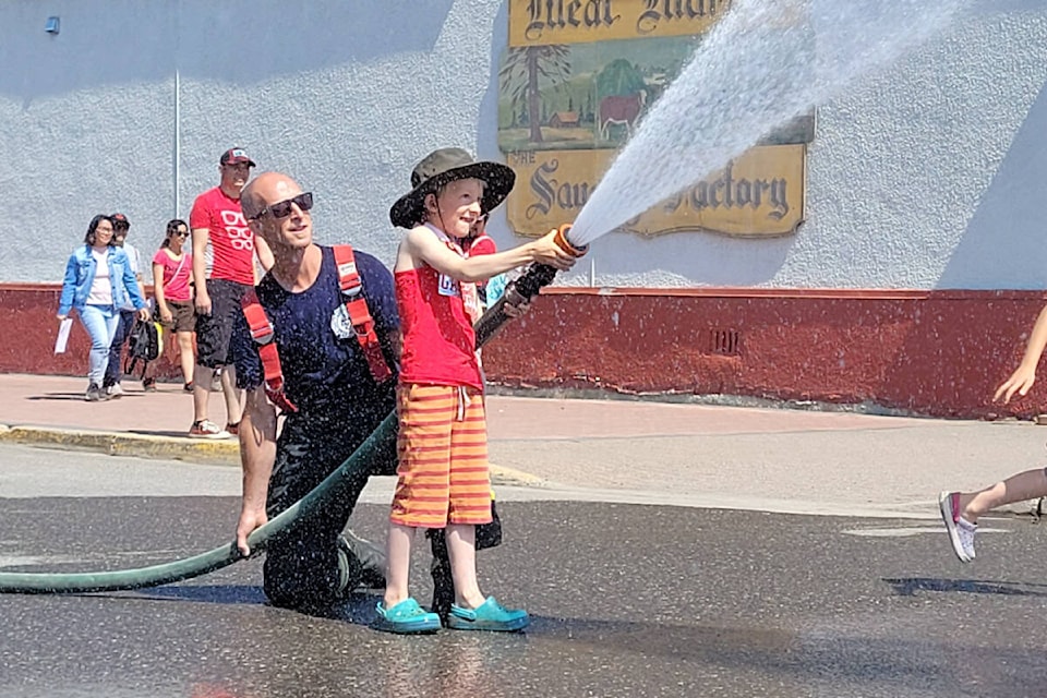 Smithers firefighter Maclean Stefanek shows Zachary Williamson how to operate a fire hose during Canada Day celebrations at Bovill Square July 1. (Thom Barker photo)