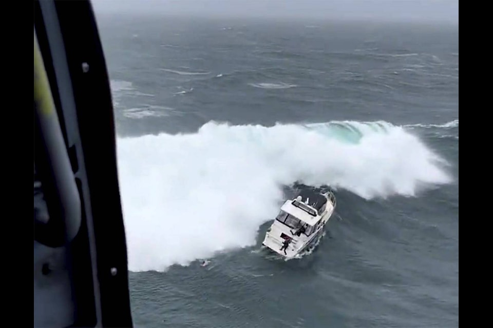 In this photo provided by the U.S. Coast Guard Pacific Northwest, a Coast Guard rescue swimmer reaches a boat right before a giant wave rolled the craft at the mouth of the Columbia River in Oregon on Friday, Feb. 3, 2023. The newly minted Coast Guard rescue swimmer saved the life of a man who was piloting the yacht. (AET1 Kyle Turcotte/U.S Coast Guard Pacific Northwest via AP)