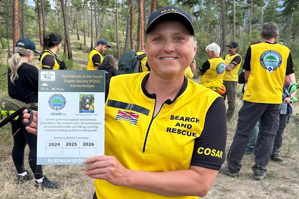 Terry Downs, Chase's handler, proudly holds the sign acknowledging the COSAR sponsorship of the Earring Trail in memory of Chase. 