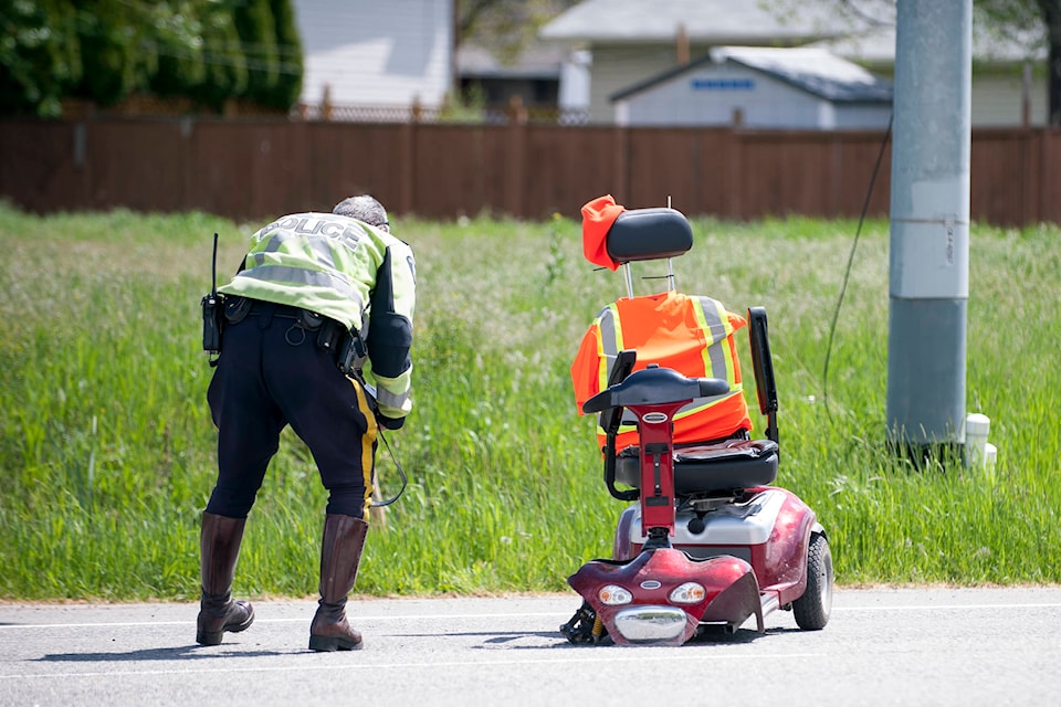 A Kelowna RCMP officer inspects an electric wheelchair after its rider collided with a vehicle along Benvoulin Road on May 13. (Michael Rodriguez - Capital News)