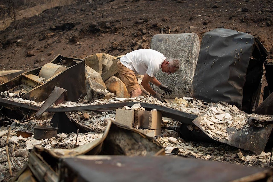 Robert Hugh looks through the remains of the home he shared with his partner Michelle Maisonneuve that was destroyed by the White Rock Lake wildfire in Monte Lake, east of Kamloops, B.C., Saturday, Aug. 14, 2021. (Darryl Dyck - The Canadian Press)