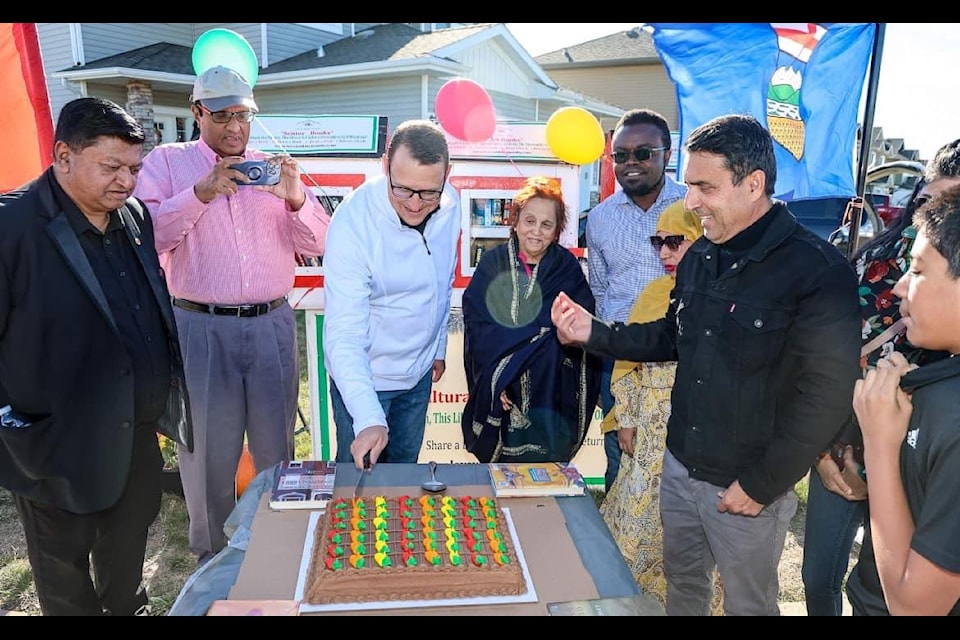 Jamie Hoover, Blackfalds mayor, cuts the celebratory cake at the opening of a multi-cultural outdoor library last weekend in town. The library is on the property of Peter Gomes (left) and was established with the help of Syed Hassan of the Calgary-based Love with Humanity Association.
(Albert Woo photo)