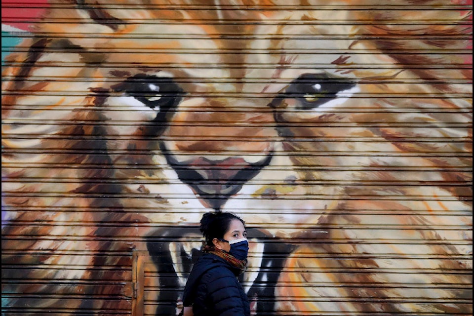 A mural decorates a closed store, where a pedestrian using a face mask walks by in Buenos Aires, Argentina, Wednesday, April 15, 2020. The use of face masks became mandatory in the capital starting Wednesday, to help contain the spread of the new coronavirus. (AP Photo/Natacha Pisarenko)