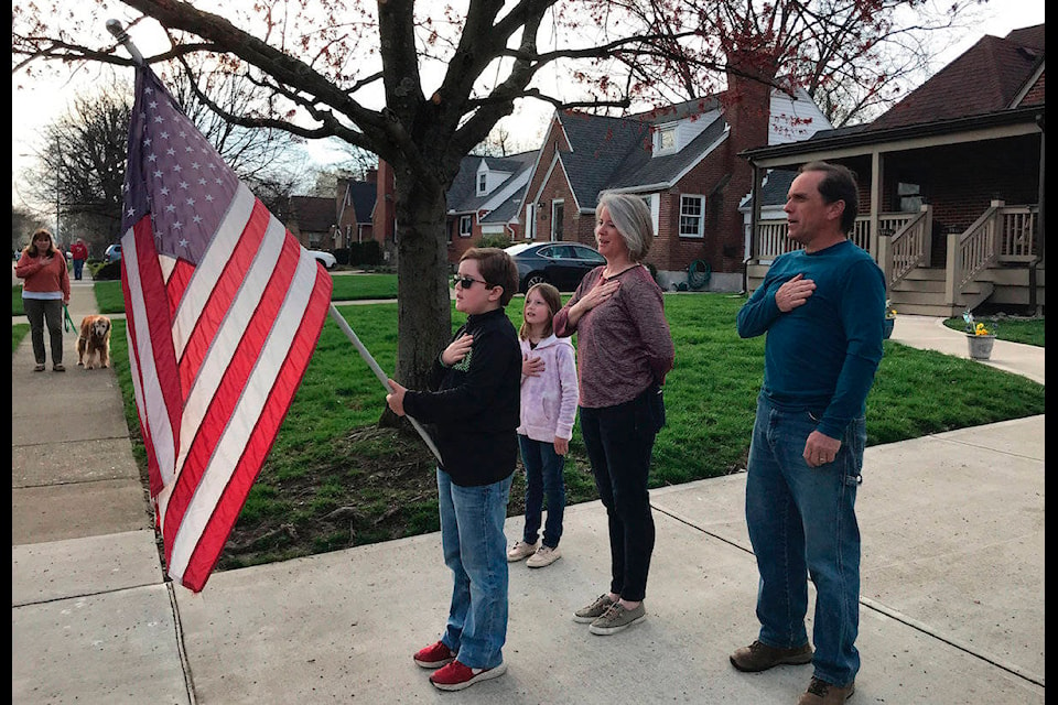 In this photo taken April 7, 2020, Zach Stamper holds the U.S. flag while his sister Juliette and parents Jennifer and Tim recite the Pledge of Allegiance in the driveway of their home, as next door neighbor, Ann Painter, left, participates in Kettering, Ohio. The Pledge has become a morning ritual in their neighborhood since schools closed due the COVID-19 threat. (AP Photo/Mitch Stacy)