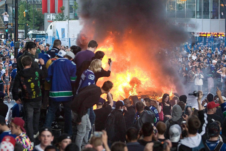 People watch a car burn during a riot following game 7 of the NHL Stanley Cup final in downtown Vancouver, B.C., in this June 15, 2011 photo. THE CANADIAN PRESS/Geoff Howe