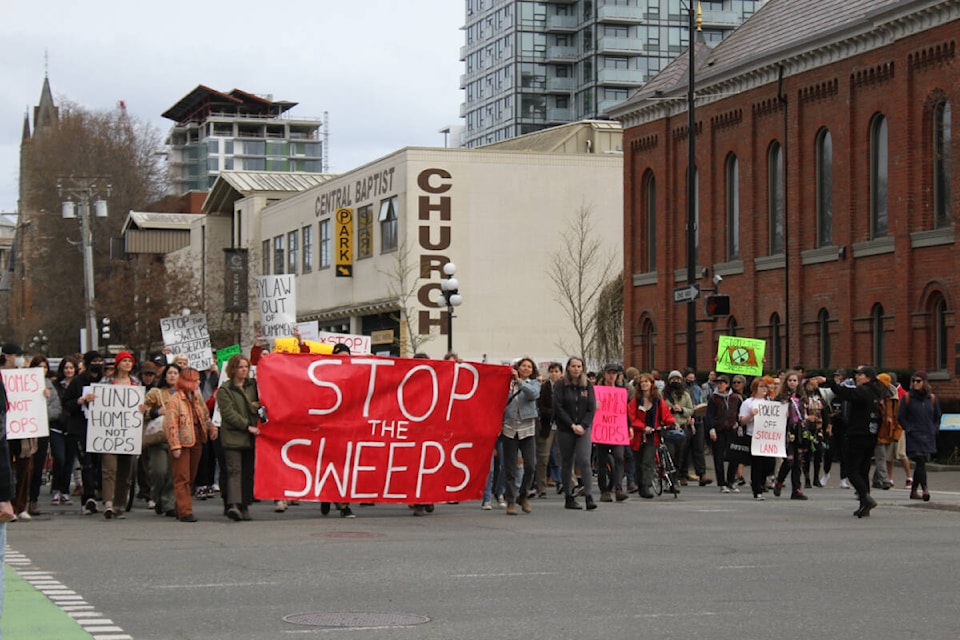 The group makes its way down Pandora Avenue toward Victoria City Hall, April 21, to call for an end to bylaw sweeps on unhoused communities. (Hollie Ferguson/News Staff)
