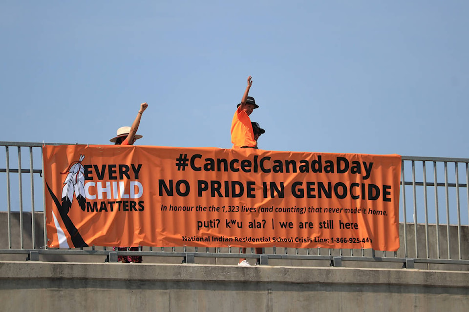 A child waves at cars by one of the banners that were dropped by members of the Westbank First Nation Youth Council (WFNYC) at the Westside Road interchange above Highway 97 in West Kelowna on July 11. (Aaron Hemens/Capital News)