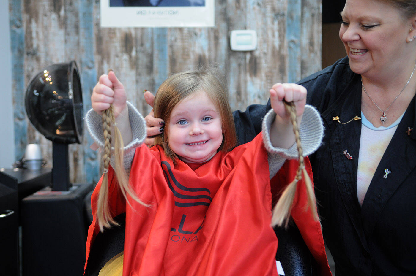 Kairi Ketler, 3, poses for a photo beside hairdresser Brenda Miller after her first haircut at Sassy Cuts on Friday, Dec. 16, 2022. Kairi is donating her 12-inch ponytails to be made into wigs for kids, and is also fundraising for charity. (Jenna Hauck/ Chilliwack Progess)