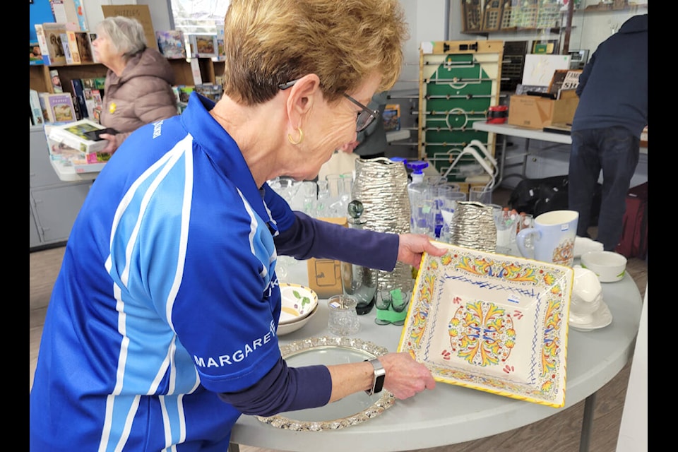 Club member Margaret Kisser inspects some of the dishware donated to the garage sale on Saturday, April 15. (Kyler Emerson/Langley Advance Times)