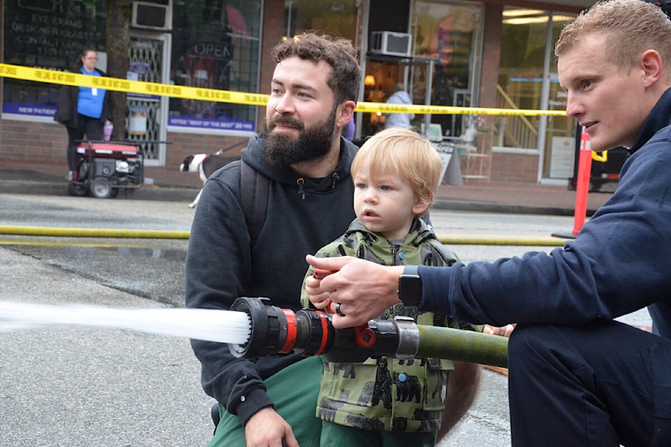 Young Mateo Jacome, one year old, with his dad Josiah and a Langley City firefighter tested out the fire hose at Langley City’s Community Day on June 10. (Matthew Claxton/Langley Advance Times)