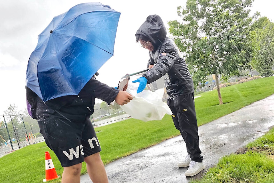 Orlando Zhang (under umbrella) and Guongdao Yang were part of a rain- and hail-drenched cleanup effort that saw more than 20 international students pick up litter in 91ԭ’s Willoughby Park near R.E. Mountain School. (Dan Ferguson/91ԭ Advance Times)