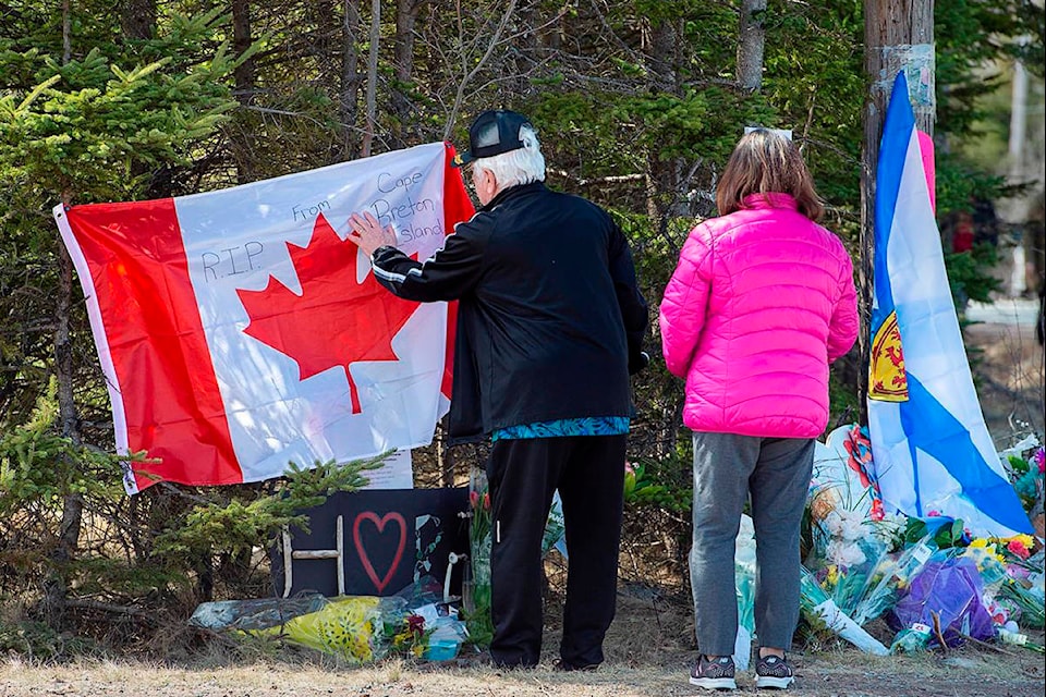A couple place a flag at a memorial in Portapique, N.S. on Wednesday, April 22, 2020. RCMP say at least 22 people are dead after a man who at one point wore a police uniform and drove a mock-up cruiser, went on a murder rampage in Portapique and several other Nova Scotia communities. THE CANADIAN PRESS/Andrew Vaughan