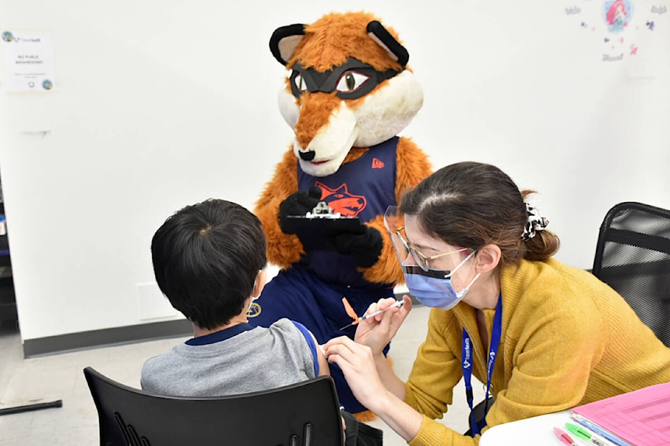 Fraser Valley Bandits mascot Berry helps out at the Maple Ridge COVID-19 vaccine clinic at Haney Place Mall on Tuesday, as a little boy received his jab from pharmacist immunizer Ana Costa. Berry was handing out stickers. (Colleen Flanagan/The News)