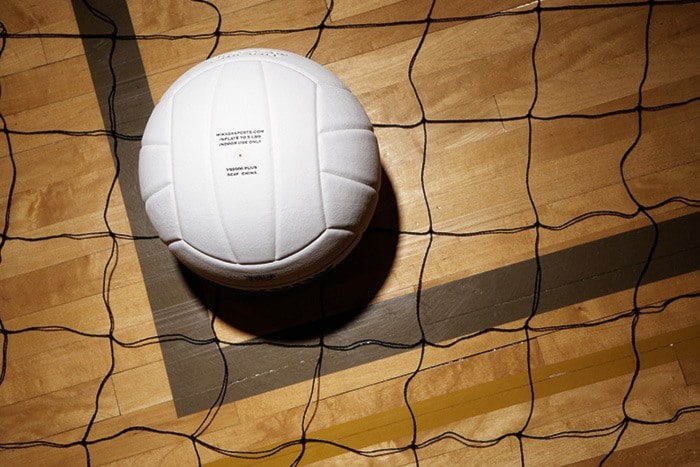 Volleyball and net on hardwood floor of volleyball court