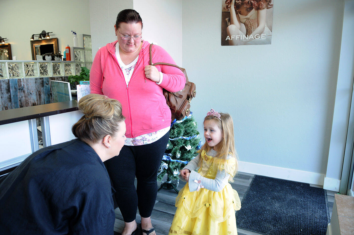 Three-year-old Kairi Ketler excitedly answers questions from Brenda Miller (left) as mom Carrie Ketler listens at Sassy Cuts on Friday, Dec. 16, 2022. Kairi had her first haircut that day and is donating her 12-inch ponytails to be made into wigs for kids, and is also fundraising for charity. (Jenna Hauck/ Chilliwack Progess)