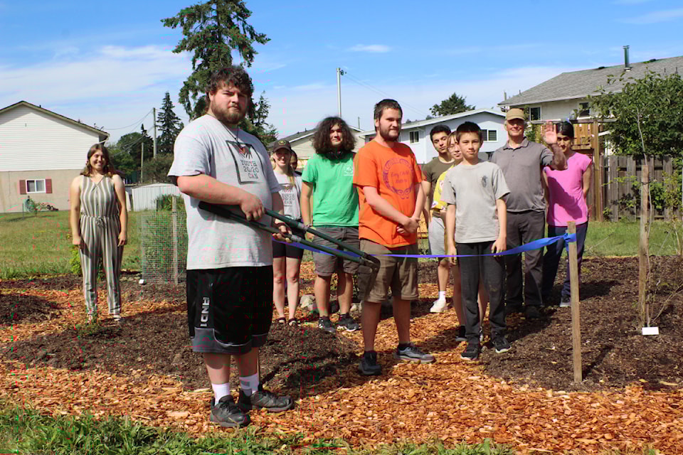 Youth 20/20 Can volunteer Justin Benvin cuts the ribbon on the new native plant garden at the food garden in Beaufort Park, with other volunteers and community members behind him.