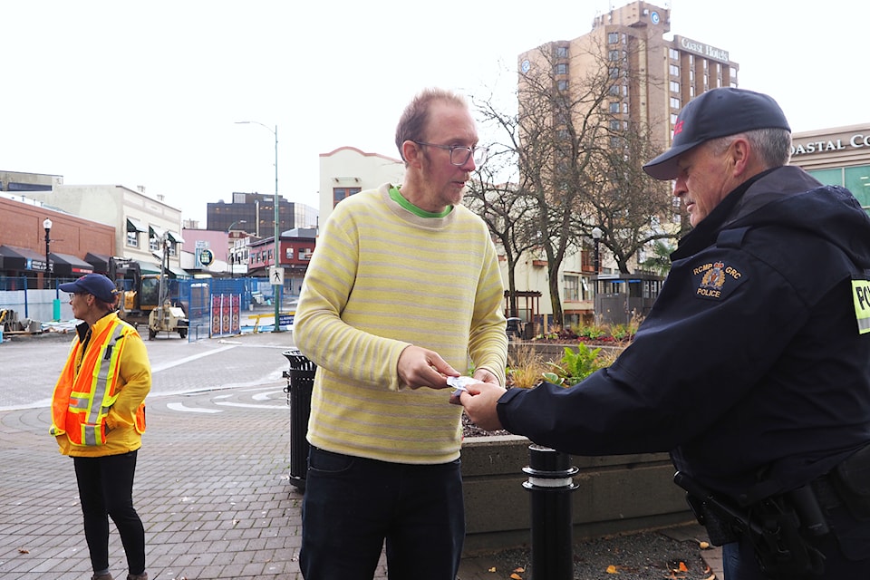 Steven Johns, owner of Red Shelf Decor, receives a reflective feather from RCMP reserve Const. Gary O'Brien as part of a city pedestrian safety promotion Wednesday,  Nov. 13. 