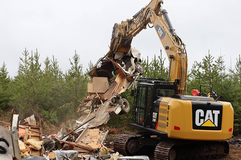 An excavator shakes debris from the frame of an RV that was left in the first up Spruston Road. (Cole Schisler photo)