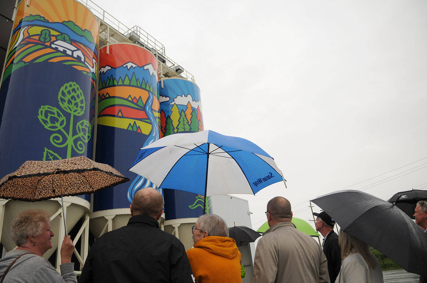 Folks check out Gifts of Nature, a public art piece installed on silos outside the Molson Coors Fraser Valley Brewery and unveiled on Thursday, June 9, 2022. The piece was designed by Chilliwack artist Silvana Kulyk. (Jenna Hauck/ Chilliwack Progress)
