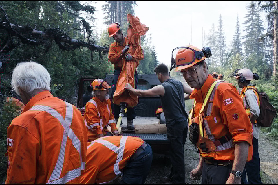 Volunteers from the Argenta fire brigade transfer water from a pillow tank to a relay tank while fighting a wildfire above their community on July 19, 2024.  