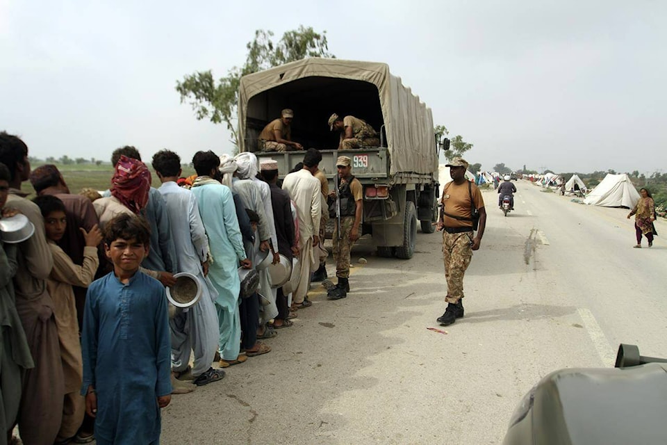 Flood affected people seen in a long queue with utensils to get food, distribute by Pakistani Army troops in a flood-hit area in Rajanpur, district of Punjab, Pakistan, Saturday, Aug. 27, 2022. Officials say flash floods triggered by heavy monsoon rains across much of Pakistan have killed nearly 1,000 people and displaced thousands more since mid-June. (AP Photo/Asim Tanveer)