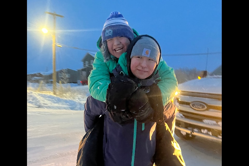 Deeandra Smith-Benoit gives her sister Della a piggyback ride. The pair joined their fellow Moose Kerr School students in welcoming back the sun back to Aklavik on Friday, Jan. 10. Photo courtesy of Colin Rose