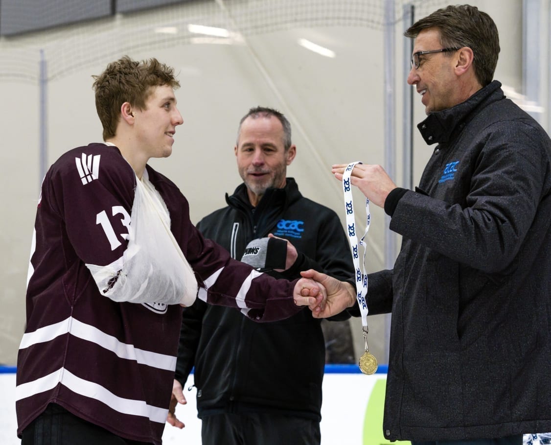 Jacob Schofield, sling and all, accepts his gold medal from Mark Kosak, chief executive officer of the Alberta Colleges Athletics Conference (ACAC), after the MacEwan Griffins men's hockey team won its third consecutive ACAC title in Edmonton on Saturday. Matthew Jacula/MacEwan Athletics photo