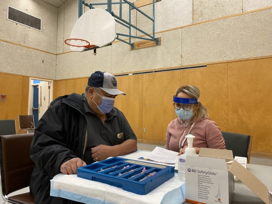 Eddie Sangris, Dettah chief of the Yellowknives Dene First Nation, left, listens as nurse Cherie Cadiz explains details of the Covid-19 vaccine to him, at Dettah's vaccination clinic on Friday. GNWT image