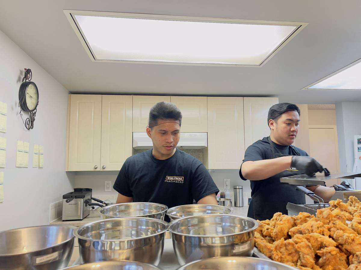 Laurence Barbosa, left, and Erick Paz prepare to apply sauce to batches of freshly deep-fried chicken wings on June 11. Photo courtesy of Wing Freak