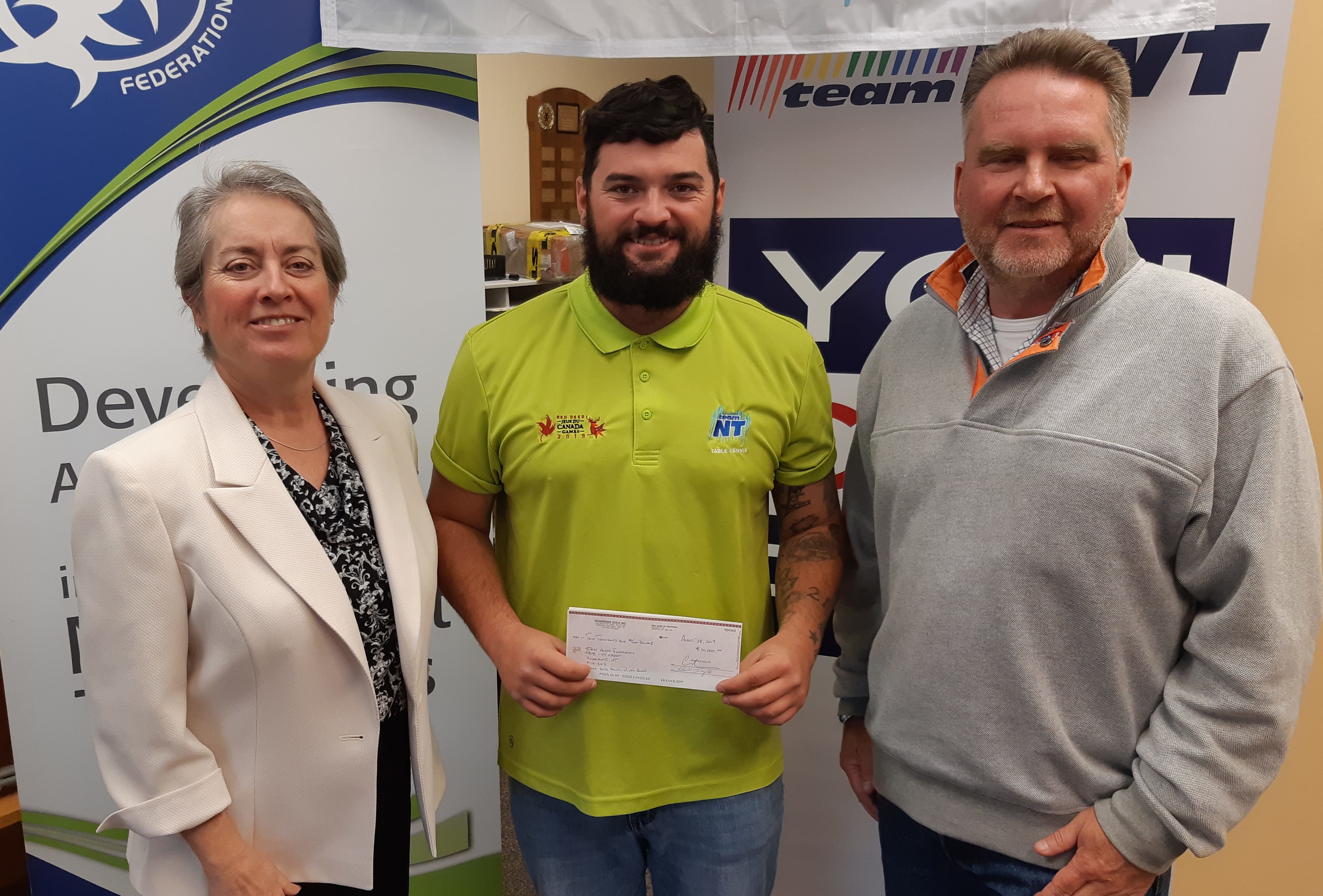 Jane Howe, left, NWT environmental manager for Seabridge Gold, and Brent Murphy, Seabridge Gold's vice-president of environmental affairs, right, present Jack Duffy, Sport North's marketing and communications officer, with a cheque for $10,000 at the Sport North offices on Aug. 29. The donation will go toward Team NT's operations for the 2020 Arctic Winter Games. James McCarthy/NNSL photo