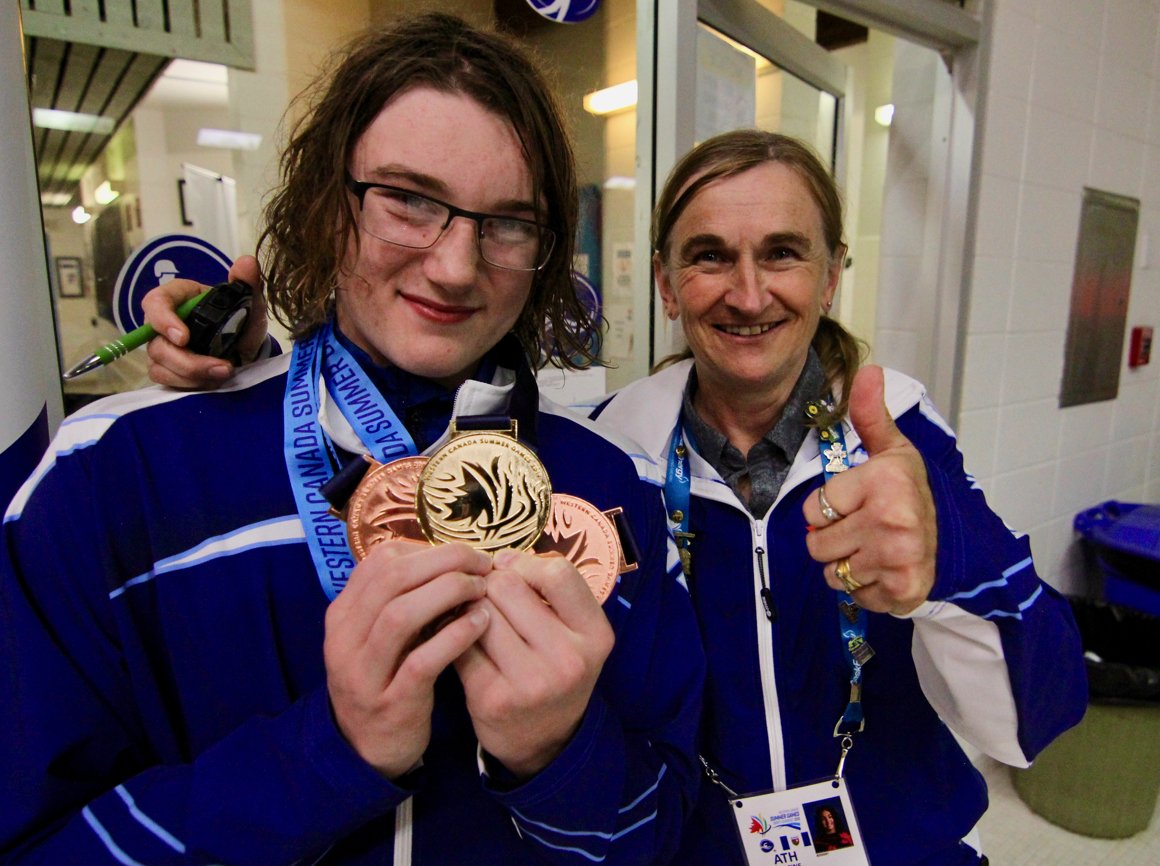 Leo Konge, left, shows off his hardware - one gold and two bronze - that hes won at the Western Canada Summer Games in Swift Current, Sask., as coach Jane Mooney gives the thumbs-up. He won gold in the 50-metre butterfly on Sunday.
