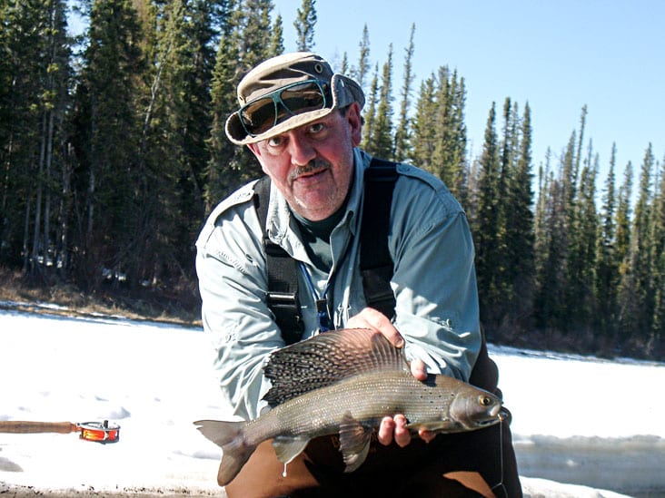 A rare photo of Mac Stark without sunglasses and holding an Arctic grayling from the Kakisa River in 2005, obviously a spawning male judging by the milt dripping from its anal fin. Mac died on Oct. 6 last year. A bench dedication ceremony will be held for him at the Kakisa River day use area on June 9. photo courtesy of John Nishi