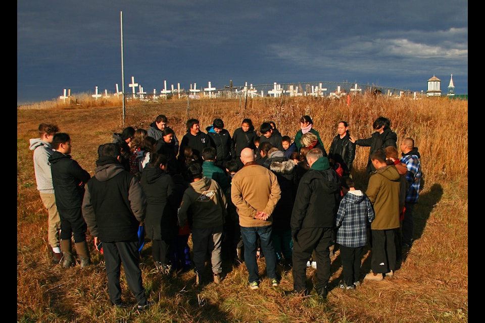 Chief Paul Niditchie School staff and students listen to a prayer in Gwich'in prior to entering cemetery grounds.