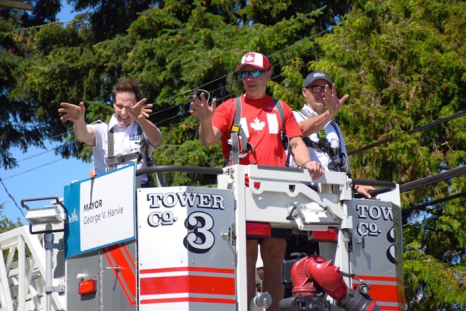 (From left) Delta Police Chief Neil Dubord, Mayor George Harvie and Fire Chief Guy McKintuck wave to the crowd from atop a firetruck as they lead the parade along 112th Street to Chalmers Park for the City of Delta's annual Canada celebration in North Delta on July 1, 2024.