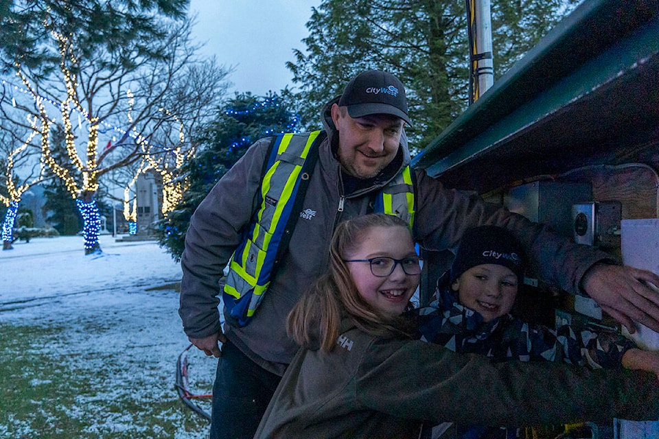 Tim Chernoff and his children, Dolly and Tommy, turn on the holiday lights around the cenotaph in front of the courthouse downtown, on Dec. 5. (Photo: Norman Galimski/The Northern View)