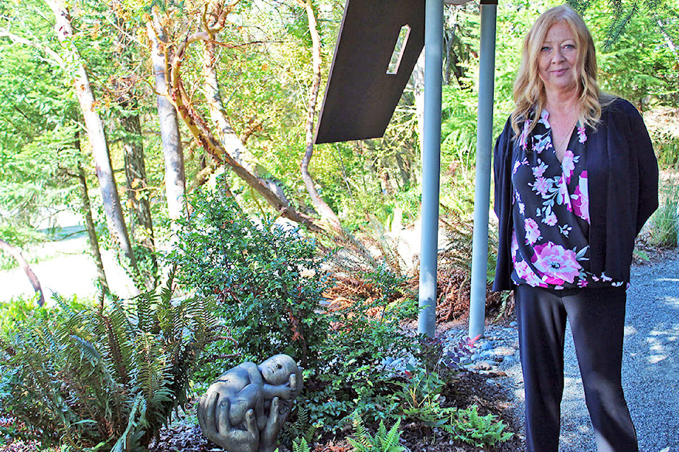 Lorraine Fracy, manager of business development and client services for the Royal Oak Burial Park, stands with a newly implemented statue in the Little Spirits Garden – one that is both raw and captures a mother’s love, she said. (Megan Atkins-Baker/News Staff)