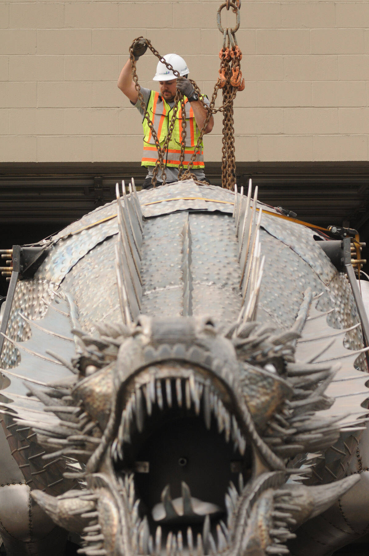 Russell Ally with Sea to Sky Transport sit on top of the massive metal dragon to hook it to a crane in preparation for its move to a new workshop near Yarrow on April 29, 2021. (Jenna Hauck/ Chilliwack Progress)
