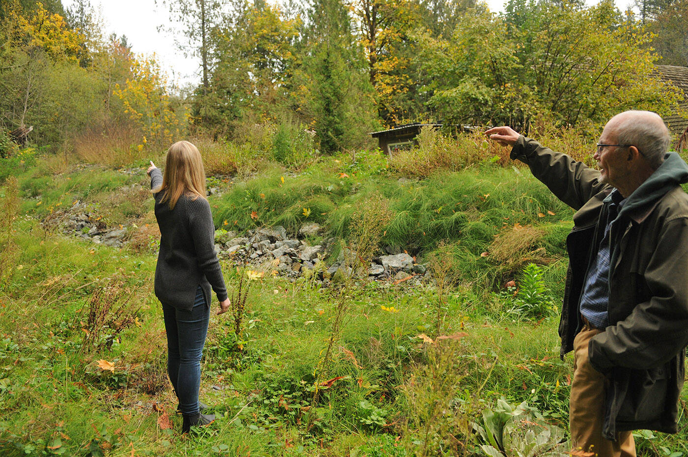 Chilliwack River Valley residents Wendy Hornberg and Richard Holmes stand on Hornbergs property on Oct. 17, 2023. After nearly two years, they and other Chilliwack River Valley residents are still without resolution after their homes were deemed unsafe to live in, or destroyed, in the floods and mudslides in November 2021. A rock berm can be seen here behind Hornbergs house (also pictured) which was installed to protect her home in case of another mudslide. (Jenna Hauck/ Chilliwack Progress)