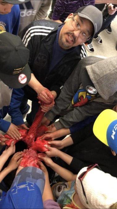 Ken Taptuna, school/community counsellor at Kugluktuk High School, is surrounded by students as he leads them in an examination the trachea and lungs of a grizzly bear.  photo courtesy of Kugluktuk High School