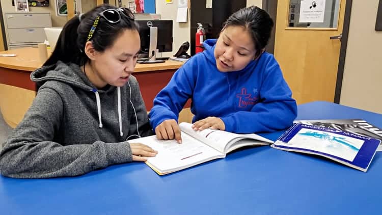 Grade 11 student Lydia Kaviok, right, discusses some of the things she learned at the Youth Parliament in Iqaluit with her friend, Edith Issakiark, at John Arnalukjuak High School in Arviat on Dec. 7, 2018. Photo courtesy Gord Billard