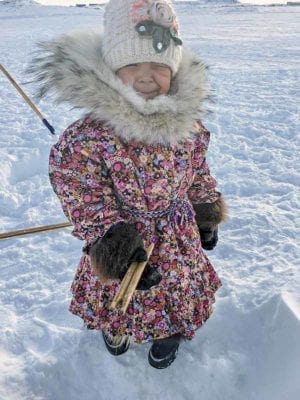 1510Alexandra Klengenberg_st.jpg<br /> Alexandra Klengenberg<br /> Kugluktuk<br /> 4-year-old Kyla Anablak fishing on 4 Mile Bay. Her parka was made last spring with Wolf Fur as a sunburst to keep warm on cold winter days.