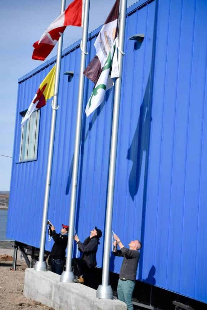 Raising the Nunavut, Canadian and Cape Dorset flags outside the Kenojuak Cultural Centre and Print Shop are, from left, Hamlet of Cape Dorset representatives Marcel Cooper and Will Sandoval along with William Huffman of West Baffin Eskimo Co-operative.