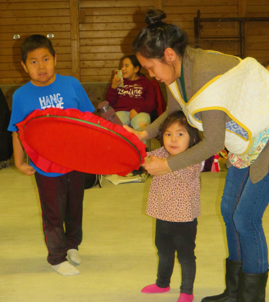 Quana Mom! I’m not too small to dance and sing, right? Mother Denica Nahogaloak assists two of her children to huqqullaaq drum dance during a practice on Tuesday, Nov. 9, 2021 in Cambridge Bay. From left, Okheena Ronald Kupeuna, 7, and little sister Palungayak Kyra Kupeuna, 2, are eager to sing and drum dance. Navalik Tologanak/NNSL photoᖁᐊᓇ ᐊᓈᓇ ! ᒥᑭᓗᐊᙱᑦᑐᖓ ᒧᒥᕐᓂᕐᒧᑦ ᐊᒻᒪ ᐃᙱᕐᓂᕐᒧᑦ, ᕼᐃᓖ ? ᐊᓈᓇᐅᔪᖅ ᑎᓂᑲ ᓇᕼᐊᒍᓗᐊᖅ ᐃᑲᔪᖅᐳᖅ ᒪᕐᕉᖕᓂ ᕿᑐᕐᙵᒥᓂᑦ ᕼᐅᖅᑯᓪᓛᕐᓂᕐᒥ ᕿᓚᐅᔾᔭᕐᓂᕐᒧᑦ ᐱᔭᕆᐅᖅᓴᓂᕐᒧᑦ ᐊᐃᑉᐹᓂ, ᓄᕕᐱᕆ 9, 2021 –ᒥ ᐃᖃᓗᒃᑑᑦᑎᐊᕐᒥ, ᓴᐅᒥᖕᒥ, ᐅᒃᕼᐄᓇ ᕌᓄᑦ ᑯᐱᐅᓇ, 7, ᐊᒻᒪ ᓇᔭᑯᓗᐊ ᐸᓗᖓᔭᒃ ᑲᐃᕋ ᑯᐱᐅᓇ , 2, ᖁᕕᐊᑉᐳᑦ ᐃᙱᕐᓂᕐᒧᑦ ᐊᒻᒪ ᕿᓚᐅᔾᔭᕐᓂᕐᒧᑦ .